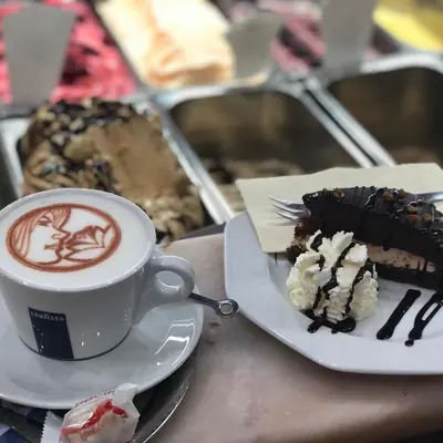 Cappuccino mit Milchschaum-Motiv neben einem Stück Schokoladenkuchen mit Sahne