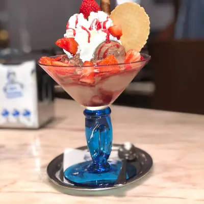 Erdbeerbecher mit frischen Erdbeeren, Sahne und Waffel im Glas auf blauem Fuß