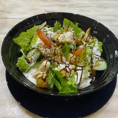 Salat mit Hähnchenstreifen und Dressing in einer dunklen Schale
