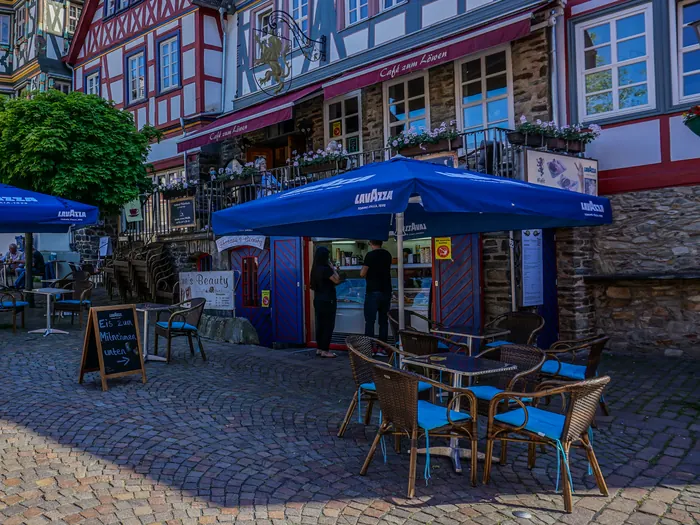 Tische und Stühle auf dem Kopfsteinpflaster vor dem Café zum Löwen, rechts das Fachwerkhaus mit Markisen